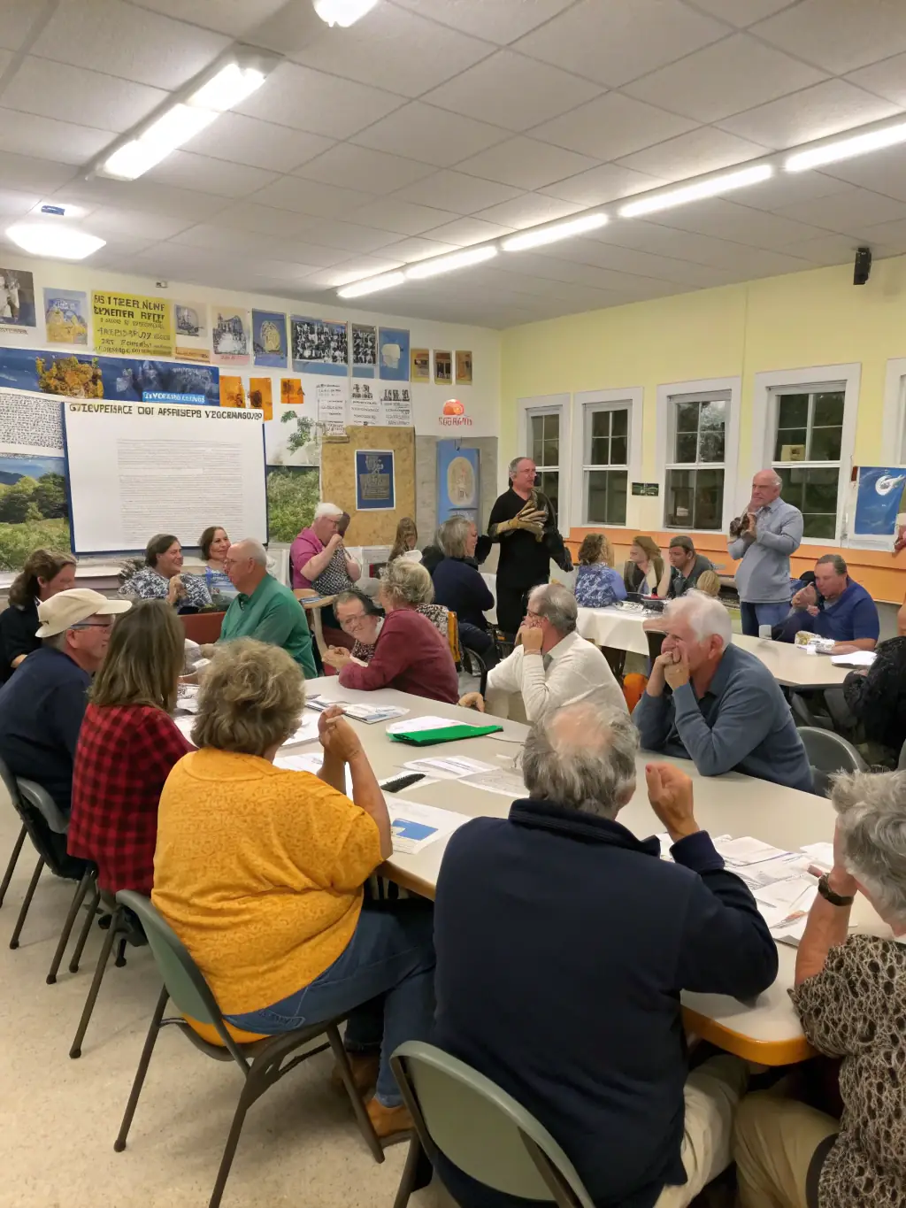 A lively town hall meeting with community members of all ages discussing local projects, with federation volunteers facilitating the conversation.